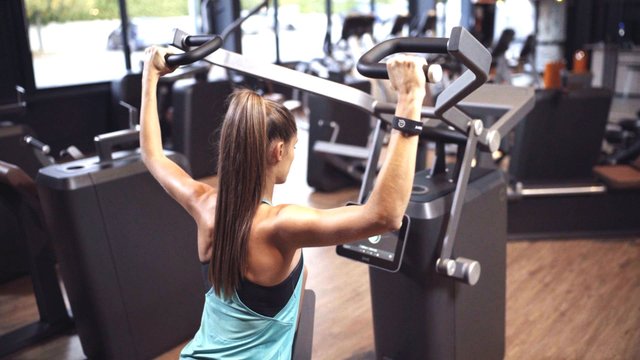 Junge Frau trainiert an der milon Q+ Schulterpresse